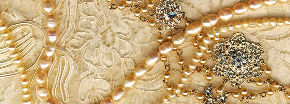 Pearl necklace and a jeweled brooch on elegant lace fabric.