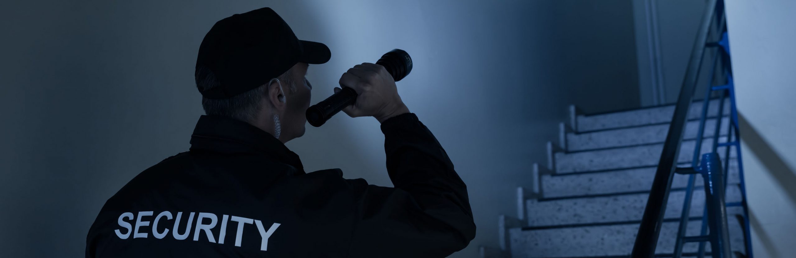 Person in dark clothing holding a flashlight in a dimly lit room.