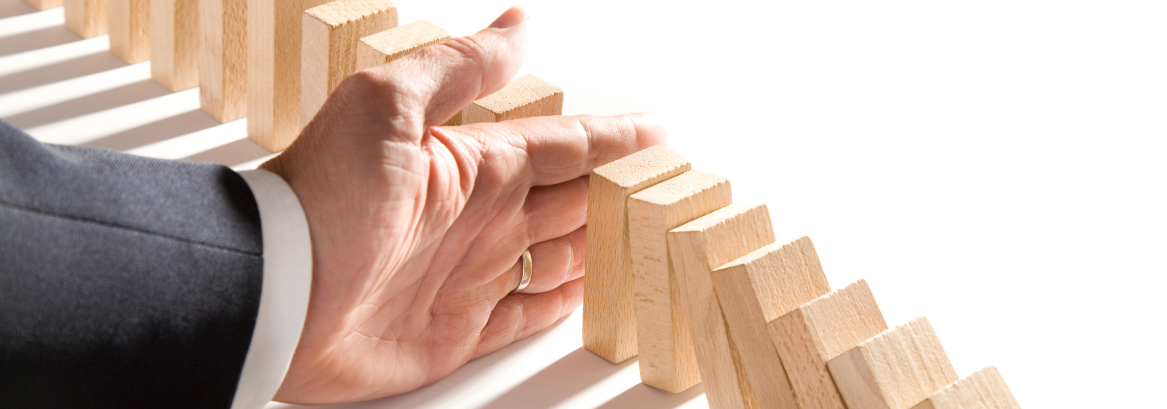 Hand stopping falling wooden domino blocks.
