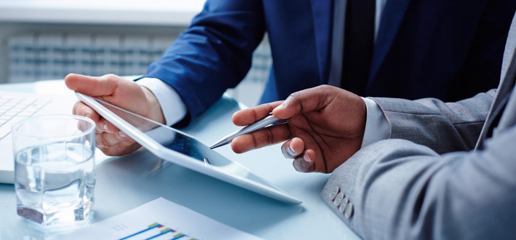 Two professionals discussing data on a tablet with documents on the table.